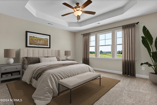 carpeted bedroom with ceiling fan and a raised ceiling