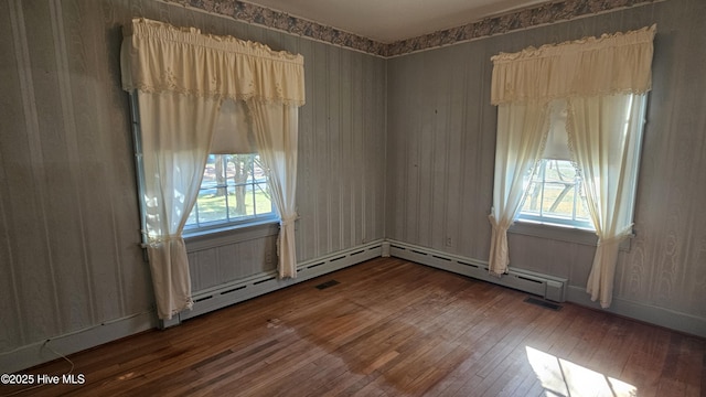 empty room featuring plenty of natural light, a baseboard heating unit, and hardwood / wood-style floors