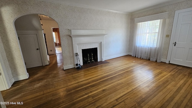 unfurnished living room with crown molding, arched walkways, a brick fireplace, and dark wood finished floors