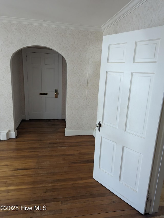 corridor featuring dark wood-style floors, arched walkways, wallpapered walls, and ornamental molding