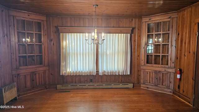 unfurnished dining area with wood ceiling, wood walls, a baseboard radiator, and wood finished floors