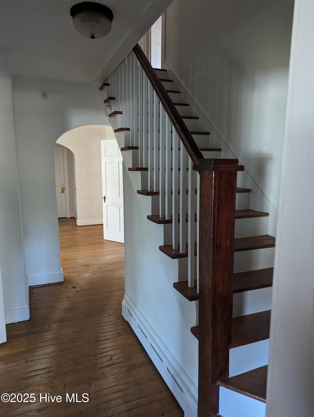 stairway featuring a baseboard heating unit, wood-type flooring, arched walkways, and baseboards