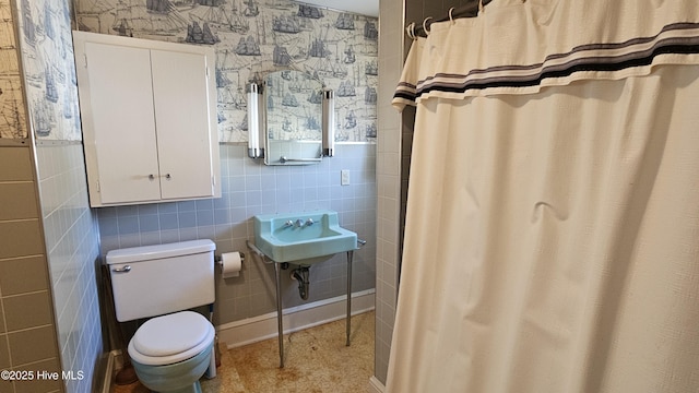 full bathroom featuring toilet, wallpapered walls, a sink, and wainscoting