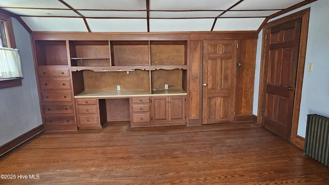 unfurnished office featuring radiator, dark wood finished floors, and built in desk