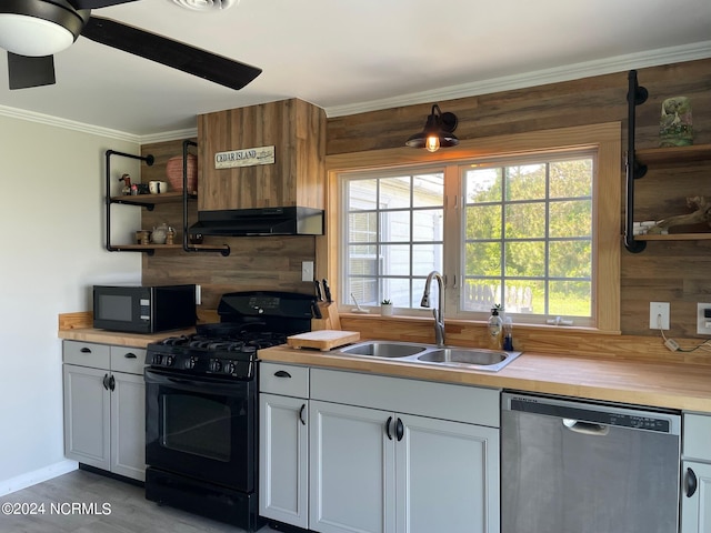 kitchen featuring wood walls, ceiling fan, black appliances, and sink