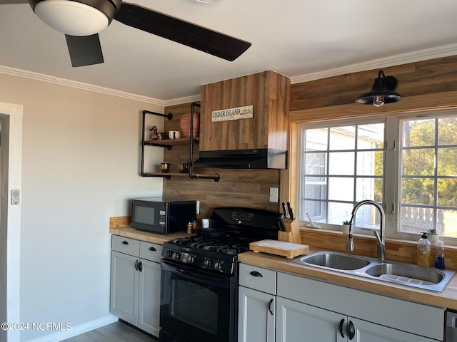 kitchen with wooden walls, black appliances, ceiling fan, and sink