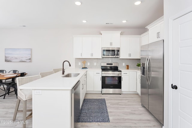 kitchen with a kitchen breakfast bar, tasteful backsplash, appliances with stainless steel finishes, white cabinets, and sink