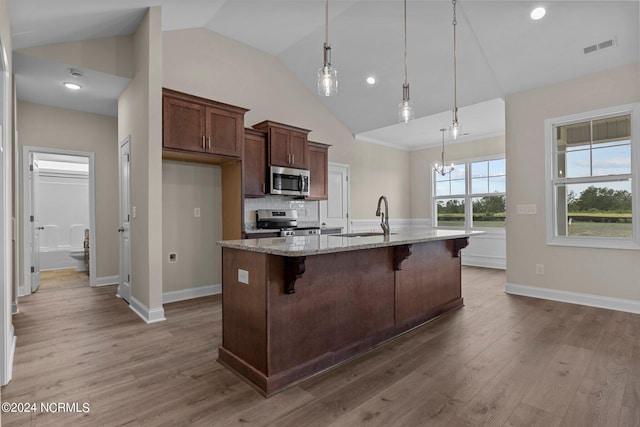 kitchen featuring a breakfast bar, pendant lighting, a kitchen island with sink, stainless steel appliances, and light stone countertops