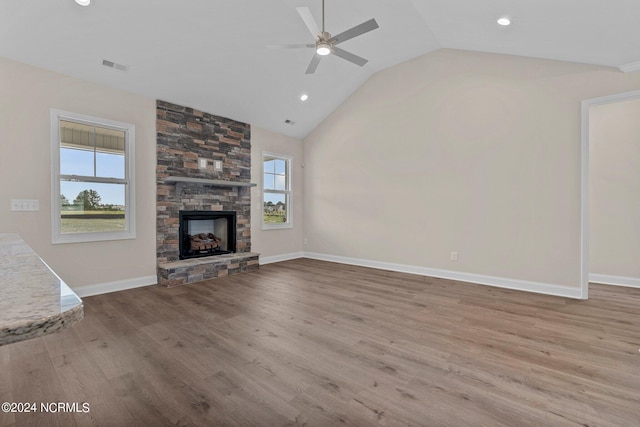 unfurnished living room with vaulted ceiling, a stone fireplace, a wealth of natural light, and light hardwood / wood-style flooring