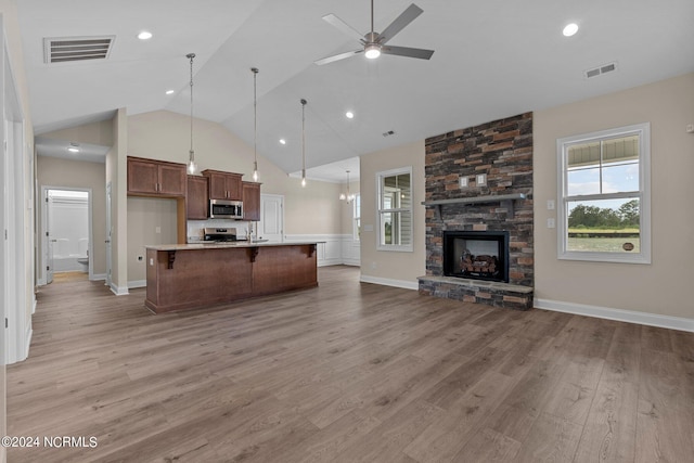 kitchen with appliances with stainless steel finishes, pendant lighting, a fireplace, a kitchen island with sink, and light hardwood / wood-style flooring