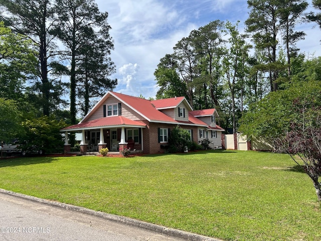 view of front of home featuring covered porch, metal roof, brick siding, and a front yard