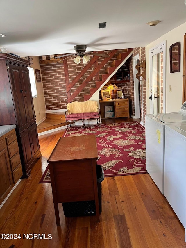 living area featuring a ceiling fan, brick wall, wood-type flooring, and washing machine and clothes dryer