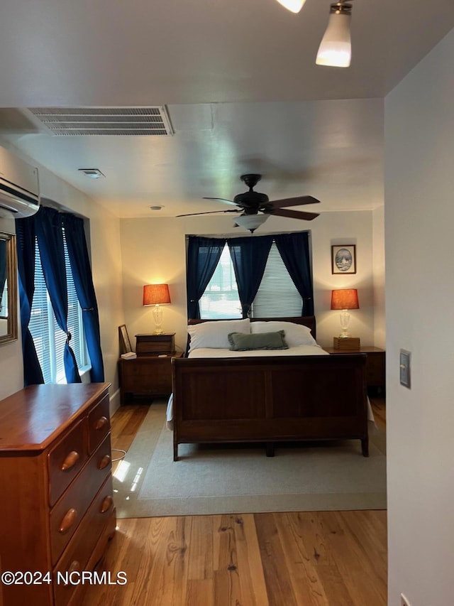 bedroom featuring visible vents, a wall mounted air conditioner, and light wood-style flooring