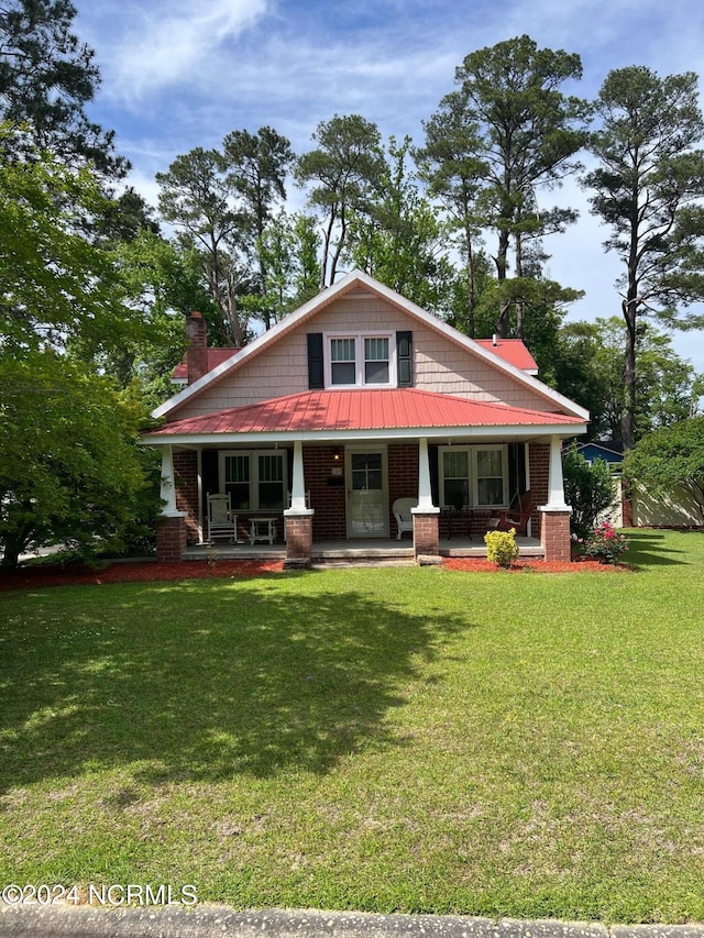 craftsman house featuring a front yard, covered porch, brick siding, and metal roof