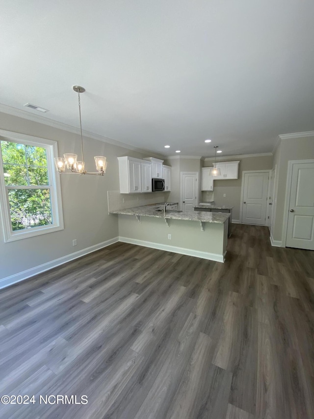 kitchen with light stone counters, dark hardwood / wood-style floors, decorative light fixtures, white cabinets, and ornamental molding