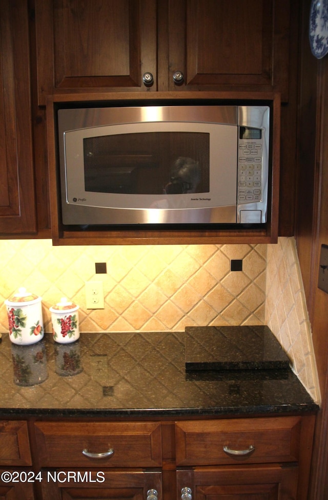 kitchen with tasteful backsplash, dark stone countertops, and stainless steel microwave