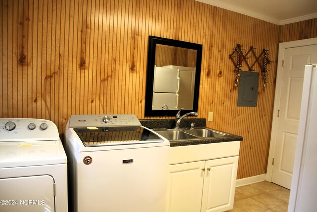 clothes washing area with wooden walls, light tile flooring, washer and clothes dryer, crown molding, and sink