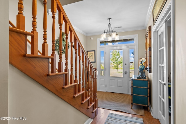 entryway featuring a chandelier, wood finished floors, visible vents, stairs, and ornamental molding