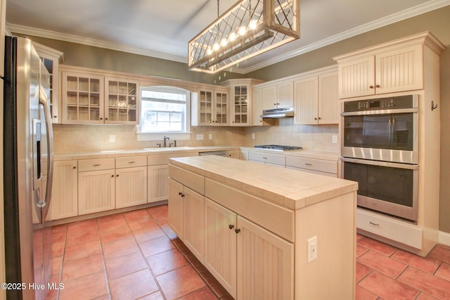 kitchen featuring a kitchen island, glass insert cabinets, decorative light fixtures, stainless steel appliances, and under cabinet range hood