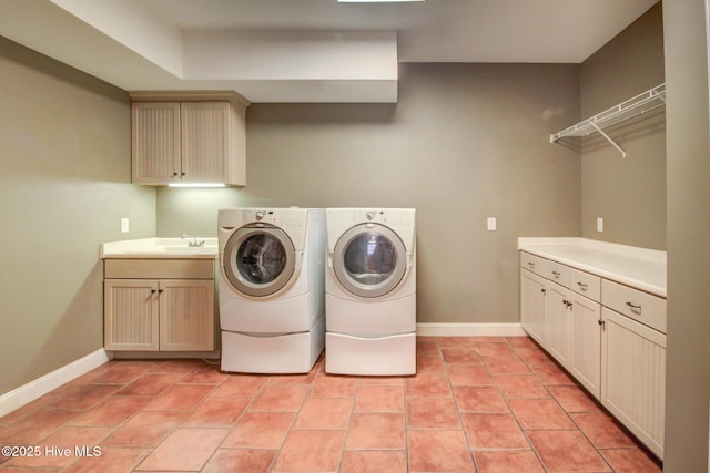 laundry area featuring light tile patterned floors, a sink, baseboards, cabinet space, and washing machine and clothes dryer