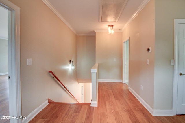 corridor with light wood-style floors, attic access, crown molding, and an upstairs landing