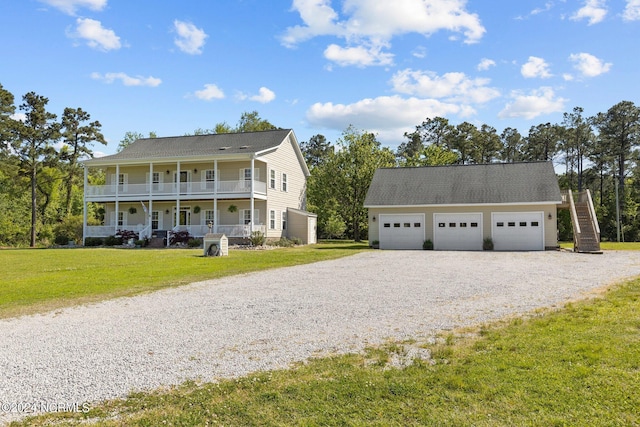 view of front of house featuring covered porch, a detached garage, a balcony, and a front lawn