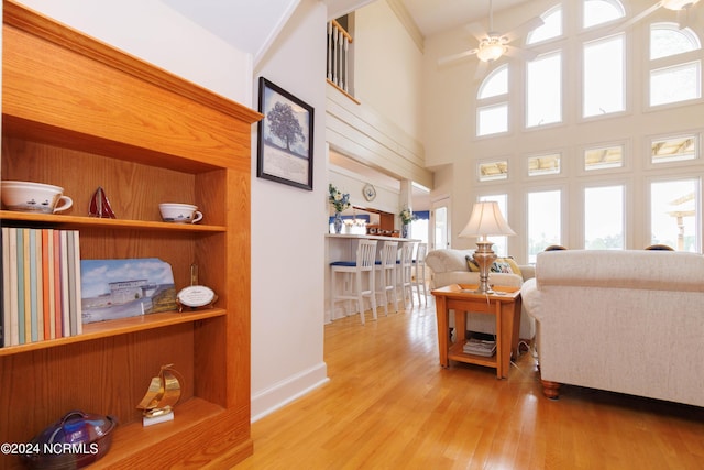 living room with built in shelves, a high ceiling, ceiling fan, light wood-type flooring, and baseboards