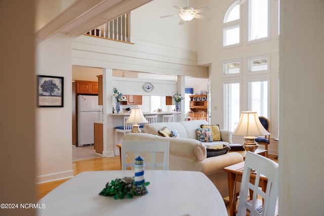 living area featuring a ceiling fan, light wood-type flooring, a healthy amount of sunlight, and a high ceiling