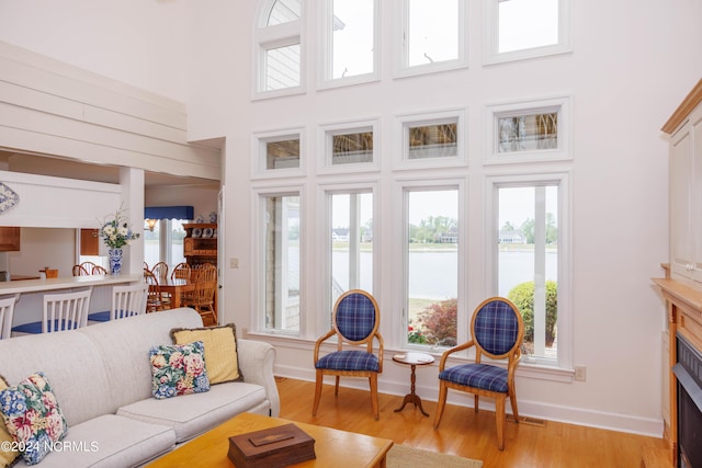 living area with a high ceiling, a water view, light wood-style flooring, and baseboards