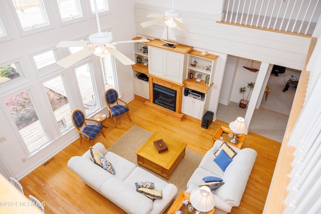 living area with visible vents, plenty of natural light, a towering ceiling, and light wood finished floors