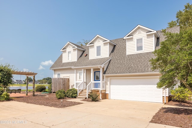 cape cod-style house with driveway, an attached garage, a pergola, and roof with shingles