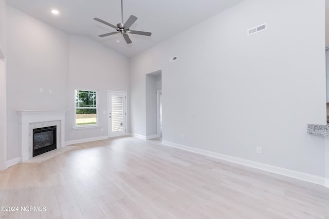 unfurnished living room with a high end fireplace, light hardwood / wood-style floors, ceiling fan, and high vaulted ceiling