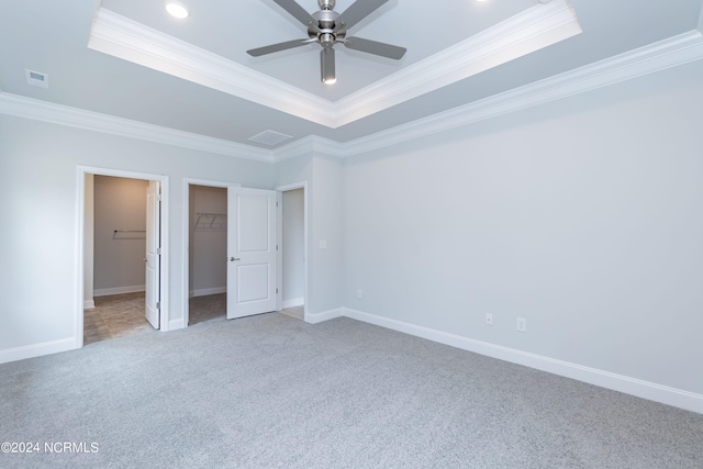 unfurnished bedroom with carpet floors, crown molding, a tray ceiling, ceiling fan, and a walk in closet