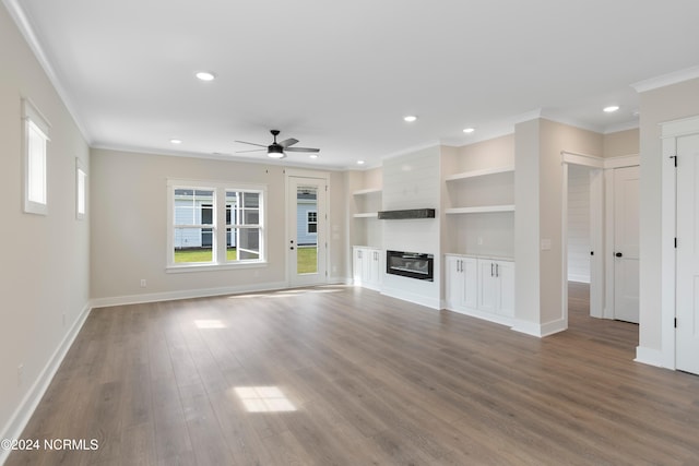 unfurnished living room featuring a large fireplace, ceiling fan, crown molding, hardwood / wood-style flooring, and built in shelves