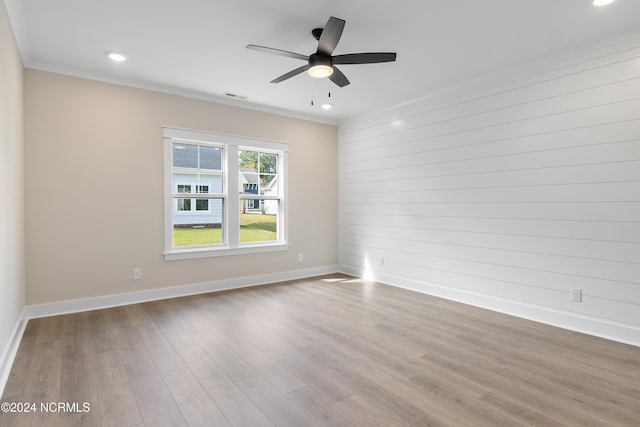 empty room featuring ornamental molding, wooden walls, light wood-type flooring, and ceiling fan