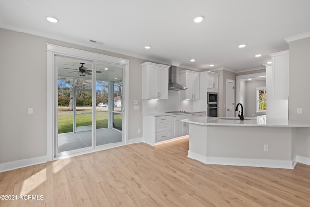 kitchen with wall chimney exhaust hood, kitchen peninsula, ornamental molding, light wood-type flooring, and white cabinets