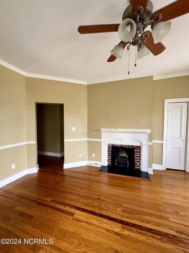 unfurnished living room with dark hardwood / wood-style flooring, a brick fireplace, ceiling fan, and crown molding