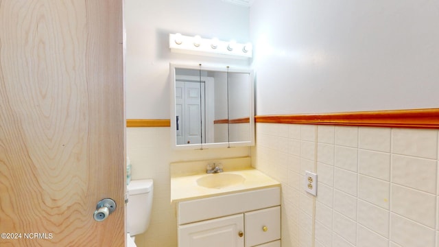 bathroom featuring vanity, toilet, and tile walls