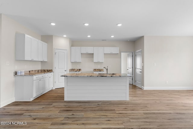 kitchen with light wood-type flooring, white cabinetry, and an island with sink