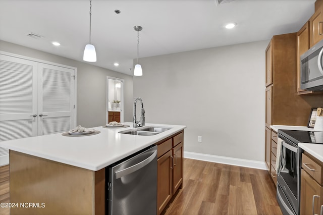 kitchen with appliances with stainless steel finishes, hardwood / wood-style floors, decorative light fixtures, sink, and a kitchen island with sink