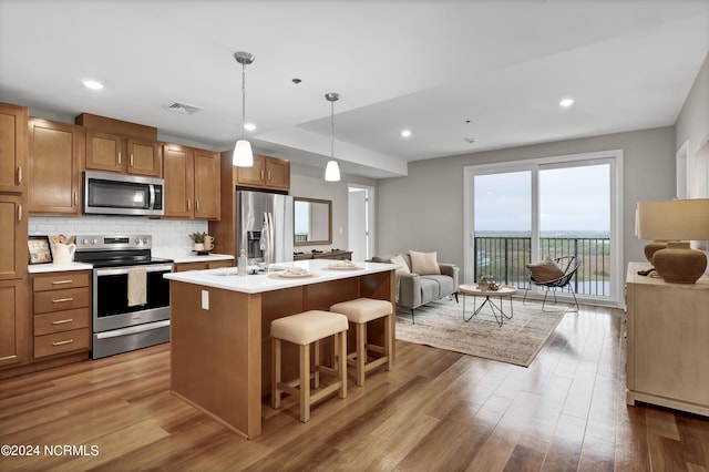 kitchen with a breakfast bar area, decorative light fixtures, stainless steel appliances, a kitchen island with sink, and decorative backsplash