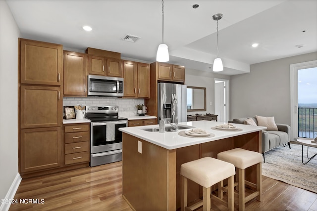 kitchen with an island with sink, a kitchen bar, decorative backsplash, hanging light fixtures, and stainless steel appliances