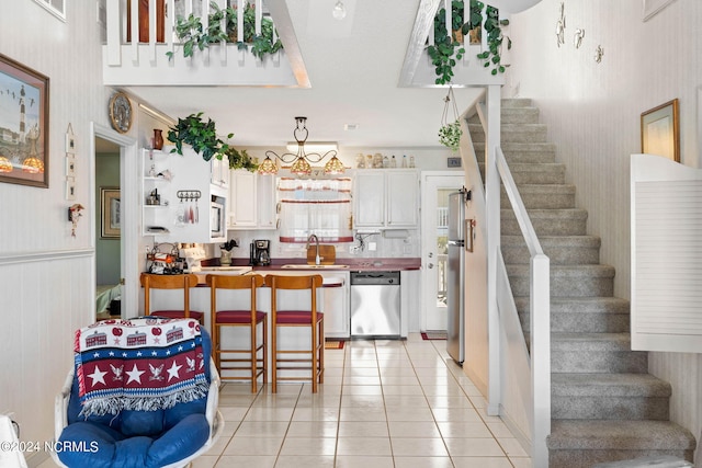 kitchen with light tile floors, white cabinets, sink, hanging light fixtures, and stainless steel appliances