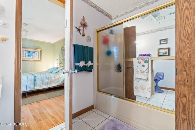 bathroom featuring tile floors, ornamental molding, combined bath / shower with glass door, ceiling fan, and a textured ceiling