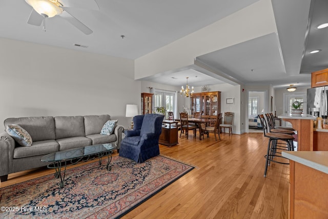 living room with a healthy amount of sunlight, ceiling fan with notable chandelier, and light hardwood / wood-style flooring