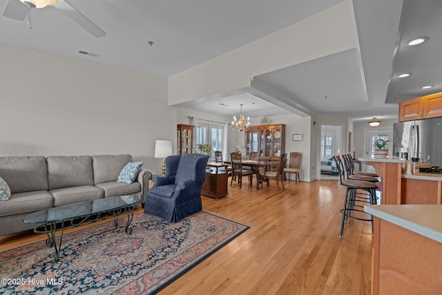 living room with ceiling fan with notable chandelier and light hardwood / wood-style flooring