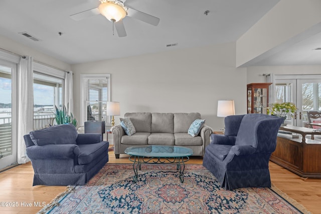 living room featuring vaulted ceiling, a wealth of natural light, light hardwood / wood-style floors, and french doors