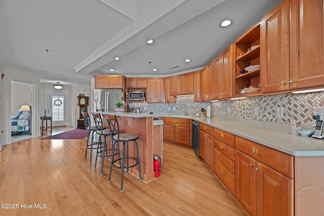 kitchen with a kitchen island, a breakfast bar area, ornamental molding, stainless steel appliances, and light hardwood / wood-style flooring