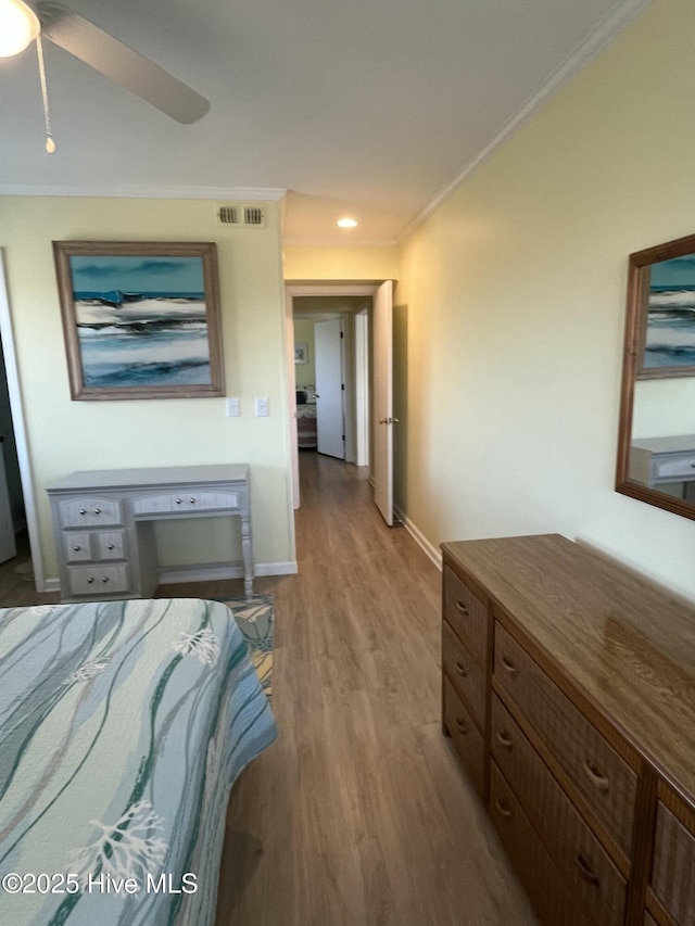 bedroom featuring wood finished floors, a ceiling fan, visible vents, baseboards, and ornamental molding