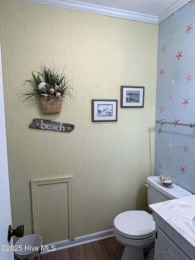 bathroom featuring baseboards, toilet, ornamental molding, wood finished floors, and vanity